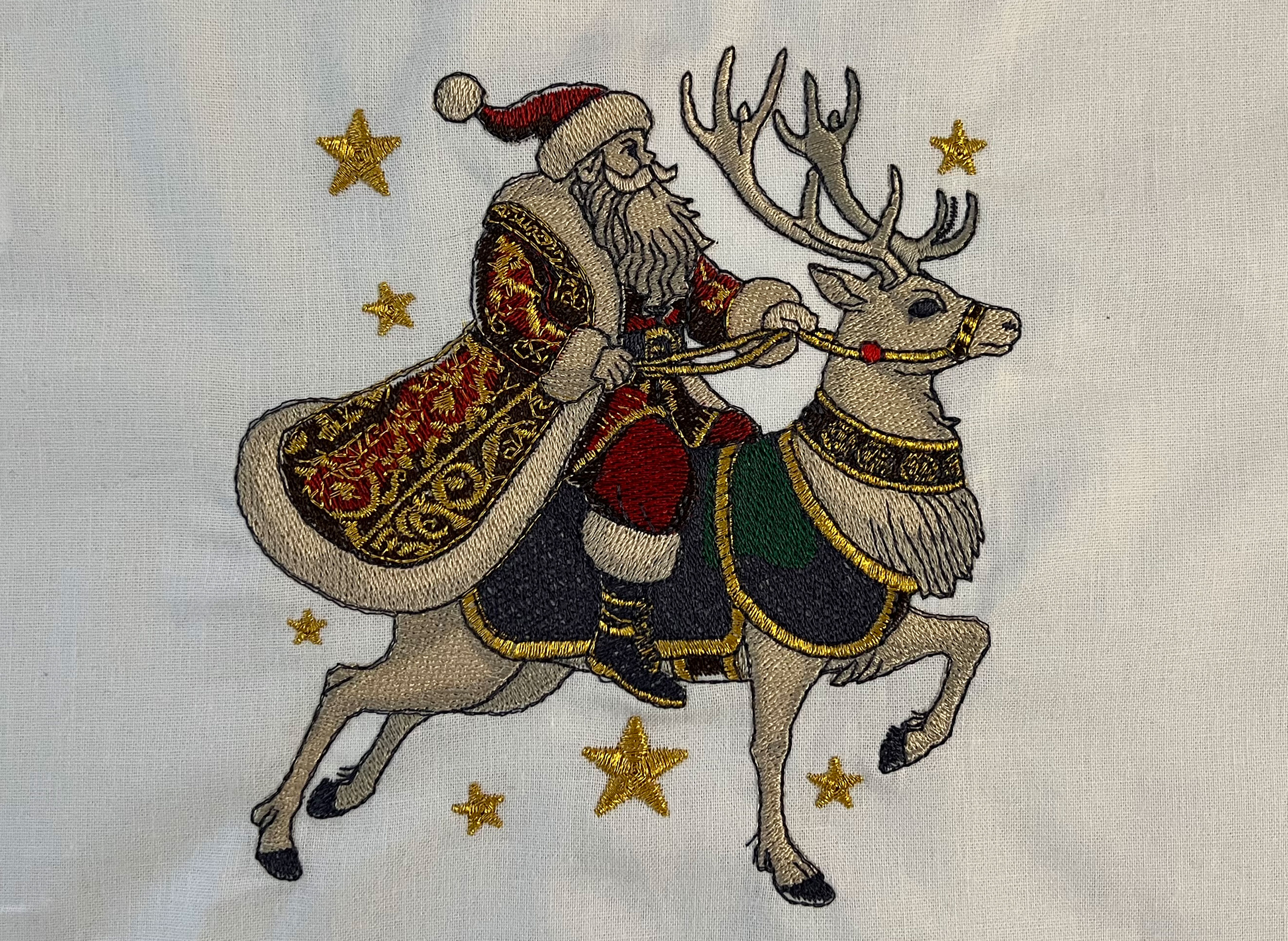 Gestickter Weihnachtsmann mit goldenem Metalik-Garn auf einem Rentier.